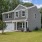 a grey home with a driveway grass and trees