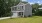 a grey home with a driveway grass and trees