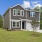 a grey home with a driveway grass and trees