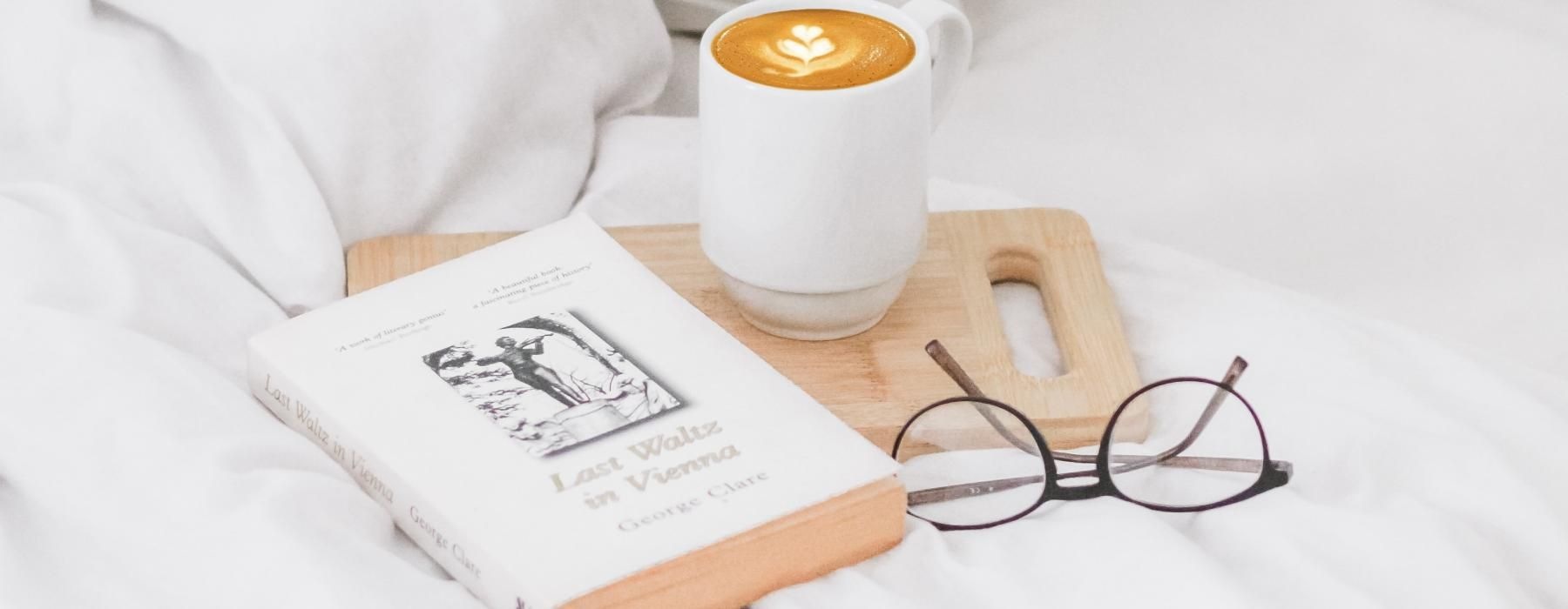 a cup of coffee a book and glasses on a bed